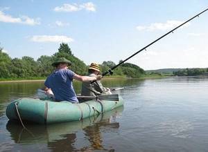 Рыболов ловит с лодки на реке с помощью удочки